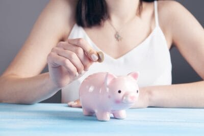 quanto rende 10 mil na poupança: mulher colocando moeda em um porquinho de moedas