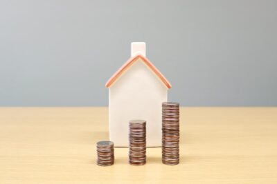 investimentos seguros: maquete de casa com três pilhas de moedas na frente