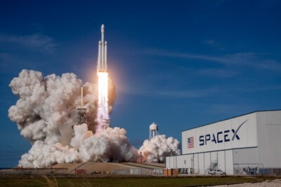 IPO da SpaceX: foguete sendo lançado próximo a um galpão com o nome 