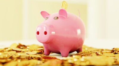 investir em renda fixa: Um cofrinho rosa cercado por uma pilha de moedas de ouro